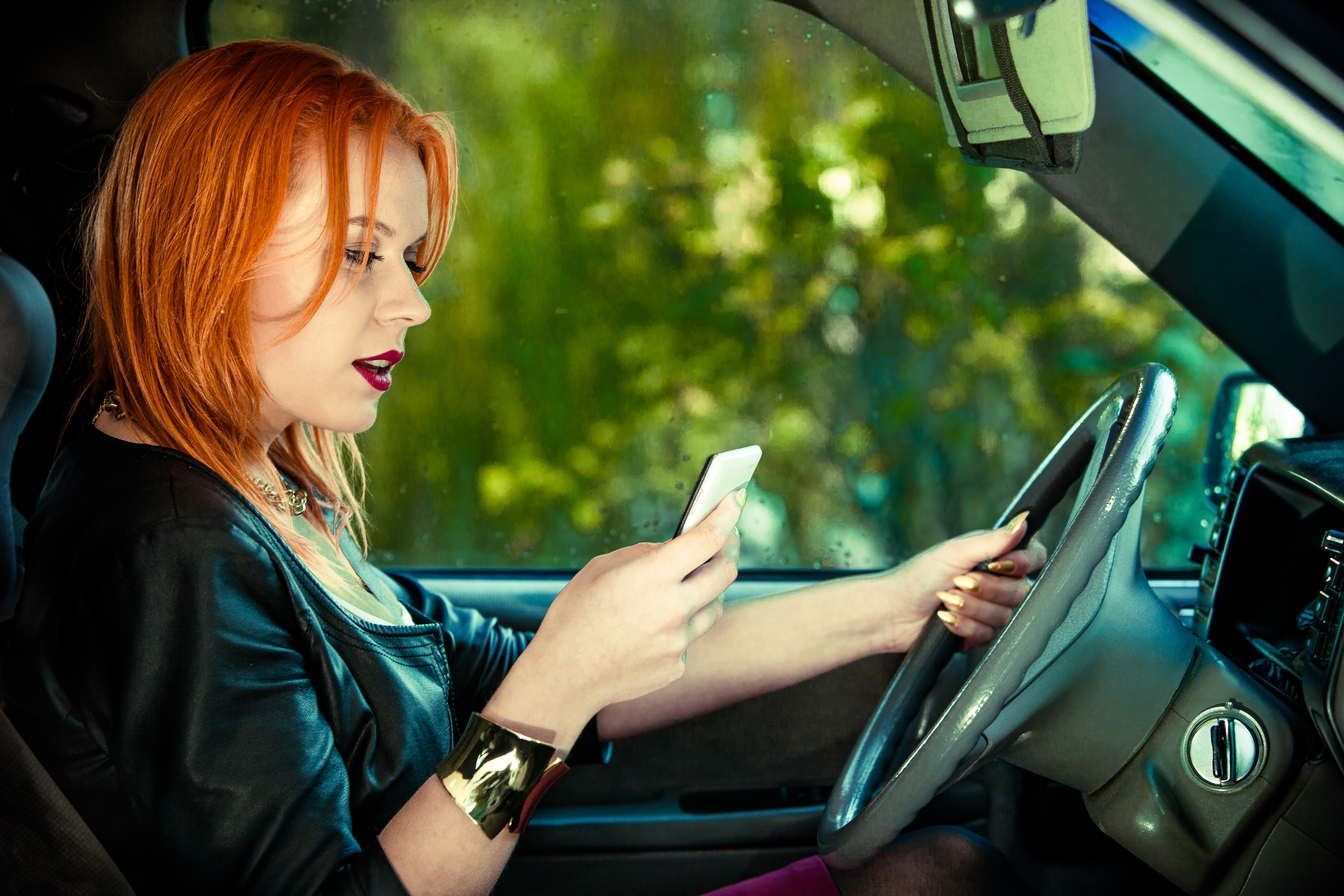 Woman driver sending text reading message on phone while driving